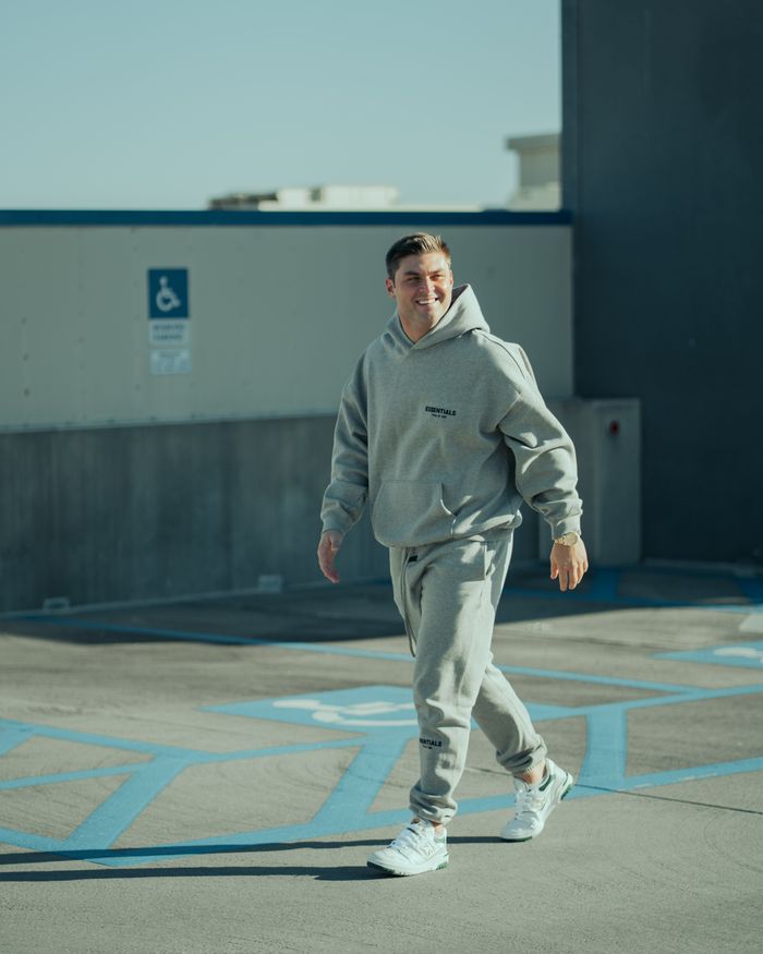 Man in gray hoodie and sweatpants walking outdoors, showcasing urban streetwear style.